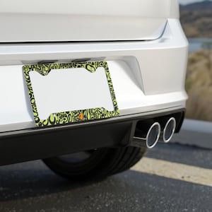 Rear license plate of a white car with exhaust piping. Green and black f1 themed lando norris car license plate frame is on the car, with personalised "4" racing number in orange. 

Lando Norris F1 License Plate Frame: Green and black pattern, Aluminum