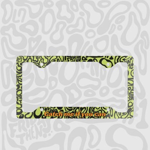 Green and black f1 themed lando norris car license plate frame is shown against a black and white lando norris pattern. Personalised phrase "catch me if you can" is shown on bottom of frame in orange mclaren themed text. 

Lando Norris F1 License Plate Frame: Green and black pattern, Aluminum