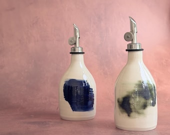 May include: Two ceramic oil dispensers with a glossy off-white finish and silver metal pour spouts. The left bottle features a solid dark blue rectangular brushstroke, while the right bottle displays a blended dark green and blue abstract mark.