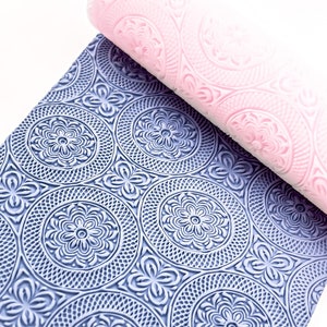 Peut inclure: Un rouleau à pâtisserie rose et un tapis de pâtisserie bleu et blanc, tous deux ornés de motifs floraux et circulaires en relief. L'ensemble crée un effet décoratif et est idéal pour la pâtisserie.