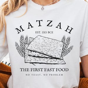 May include: White t-shirt with a graphic of matzah, the text "Matzah Est. 1313 BCE" and the text "The First Fast Food No Yeast. No Problem."
