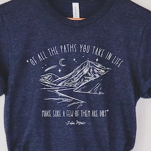 May include: A navy blue t-shirt with a white mountain graphic and the quote "Of all the paths you take in life, make sure a few of them are dirt" by John Muir.