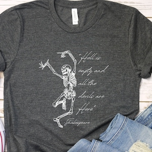 Puede incluir: Una camiseta gris oscuro con un gráfico de esqueleto blanco y la cita "El infierno está vacío y todos los demonios están aquí" atribuida a Shakespeare.