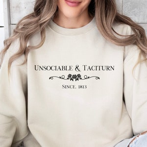 Puede incluir: Una sudadera de color crema con el texto "Unsociable & Taciturn Since 1813" impreso en negro.