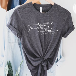 May include: A dark gray t-shirt with a white graphic design of a branch with birds and the text "The earth has music for those who listen."