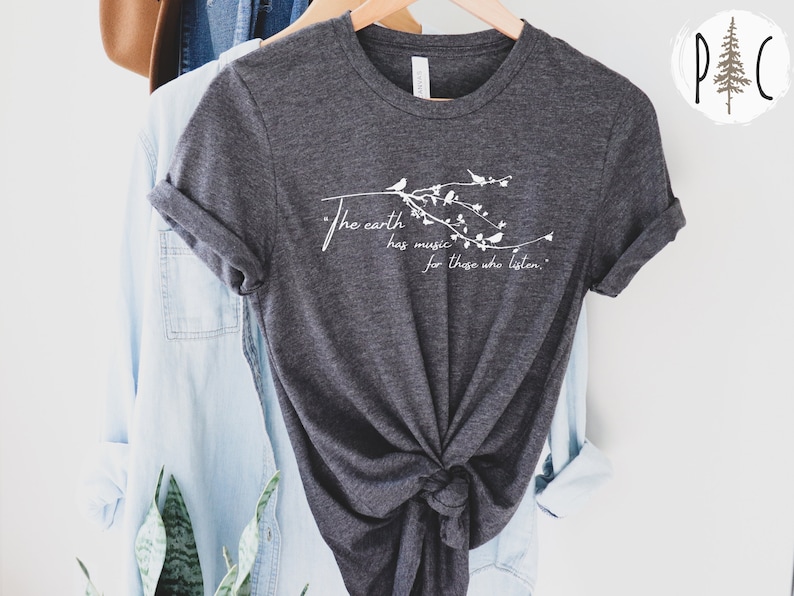 May include: A dark gray t-shirt with a white graphic design of a branch with birds and the text "The earth has music for those who listen."