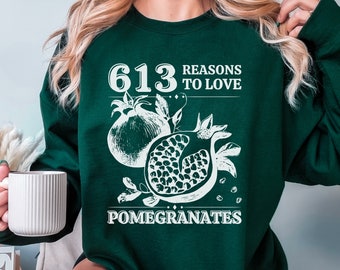 May include: Dark green sweatshirt with a white graphic of pomegranates and the text "613 REASONS TO LOVE POMEGRANATES". The design features a whole pomegranate and a sliced pomegranate.