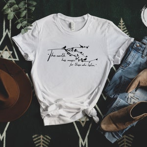 May include: White t-shirt with a black graphic of a branch with birds and the text "The earth has music for those who listen."