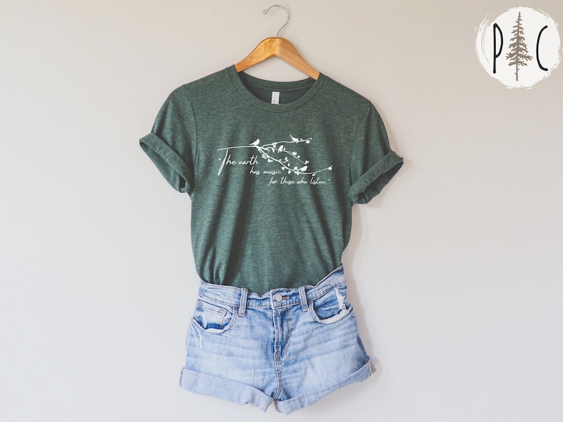 May include: A green t-shirt with a white graphic that says "The earth has music for those who listen". The graphic also includes a branch with birds and leaves.