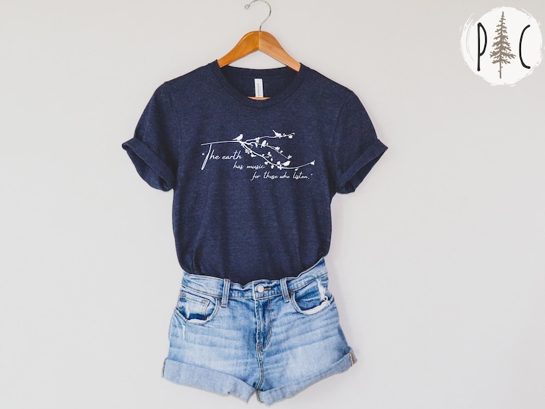 May include: A navy blue t-shirt with a white graphic print of a branch with birds and the text "The earth has music for those who listen."