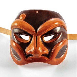 Puede incluir: Una m&aacute;scara de cuero marr&oacute;n y naranja con un rostro humano estilizado. La m&aacute;scara tiene una nariz grande y cejas exageradas.