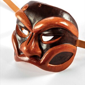 Puede incluir: Una m&aacute;scara de cuero marr&oacute;n y negro con una expresi&oacute;n dram&aacute;tica. La m&aacute;scara tiene una nariz grande y prominente y cejas exageradas. La m&aacute;scara est&aacute; dise&ntilde;ada con una correa para llevarla.