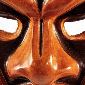 Puede incluir: Primer plano de una m&aacute;scara de cuero con una expresi&oacute;n feroz. La m&aacute;scara est&aacute; pintada en tonos marrones y negros, con una nariz prominente y ojos exagerados.