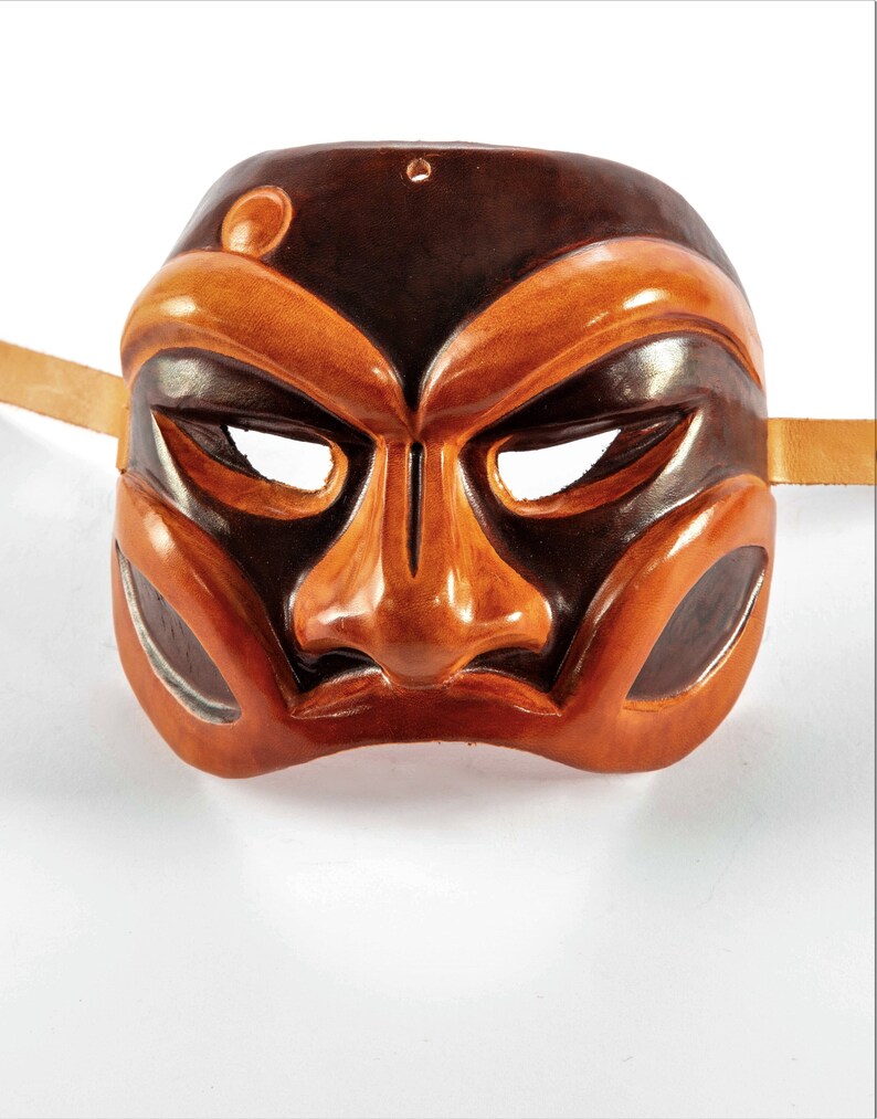 Puede incluir: Una m&aacute;scara de cuero marr&oacute;n y naranja con un rostro humano estilizado. La m&aacute;scara tiene una nariz grande y cejas exageradas.