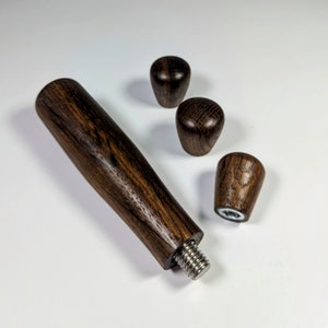 Könnte beinhalten: Ein Holz-Espresso-Tamper mit einem Gewindegriff und drei austauschbaren Holzgriffen. Der Tamper ist aus dunklem Holz mit natürlicher Maserung.