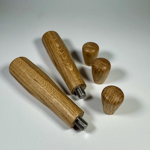 Könnte beinhalten: Zwei Holzgriffe mit Gewindeenden aus Metall und drei Holzknöpfe. Die Griffe haben ein dekoratives Muster aus Kreisen und Linien.