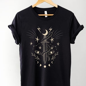 May include: Black t-shirt featuring a gold graphic design of a sword, snake, moon, and stars.