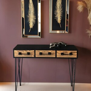 May include: A black console table with three drawers and hairpin legs. The drawers are made of wood with a natural finish. The table is decorated with a gold figurine of a leopard.