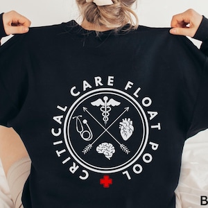 Peut inclure: Sweat-shirt noir avec un motif circulaire blanc au dos. Le motif comprend des symboles médicaux, les mots "CRITICAL CARE FLOAT POOL" et une croix rouge. Le mot "BLACK" est dans le coin inférieur droit.
