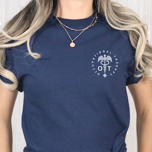 May include: A navy blue t-shirt with a white graphic of a caduceus symbol inside a circle with the text "Occupational Therapy OT" around it.