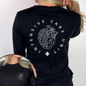May include: Black long-sleeve shirt with a white graphic on the back. The graphic features a stylized heart and brain design encircled by the words "INTENSIVE CARE UNIT" and a cross symbol. The shirt is a solid black color.