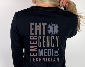 May include: Black long-sleeve shirt with the words "EMT EMERGENCY MEDICAL TECHNICIAN" printed vertically in a gradient of gray and brown. A gray star of life emblem is above the word "CAL".
