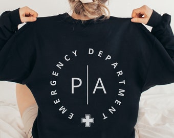 May include: Black sweatshirt with a white circle graphic on the back. The graphic says "Emergency Department" with a white cross and the letters "PA" in the center.