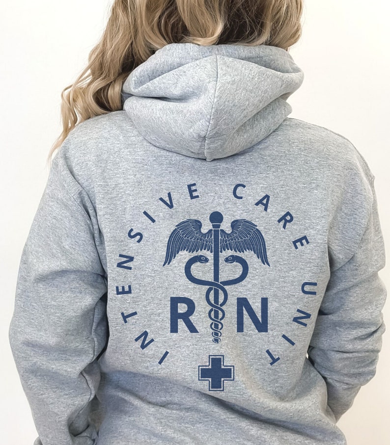 Peut inclure: Sweat-shirt &agrave; capuche gris avec un motif bleu repr&eacute;sentant un symbole m&eacute;dical, un serpent enroul&eacute; autour d'un b&acirc;ton avec des ailes, et les lettres "RN" dans un cercle. Le texte "INTENSIVE CARE UNIT" entoure le symbole.