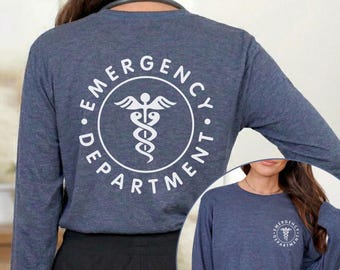 May include: A heather navy long-sleeve shirt featuring a large white circular graphic on the back with a caduceus symbol and the text EMERGENCY DEPARTMENT. A smaller version of the same circular graphic is printed on the front left chest area.