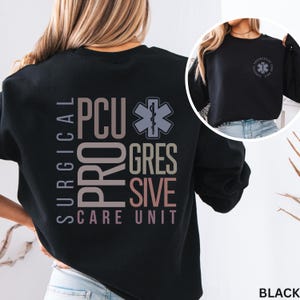 May include: A black crewneck sweatshirt featuring a large graphic on the back with the text SURGICAL PCU PROGRESSIVE CARE UNIT and a medical star of life symbol. A smaller version of the same circular logo is printed on the front left chest.