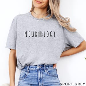 K&ouml;nnte beinhalten: Ein hellgraues T-Shirt mit dem Wort "NEUROLOGIE" in Schwarz aufgedruckt, mit einer Gehirngrafik. Das Shirt besteht aus einem weichen Material und eignet sich f&uuml;r Freizeitkleidung. Der Text "SPORT GREY" ist unten aufgedruckt.