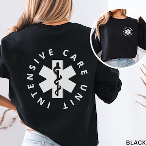 以下が含まれることがあります： 黒のクルーネックトレーナー。背中には「INTENSIVE CARE UNIT」の文字とスター・オブ・ライフのシンボルが大きく白でプリントされています。左胸にも同じデザインの小さな白いロゴがプリントされています。