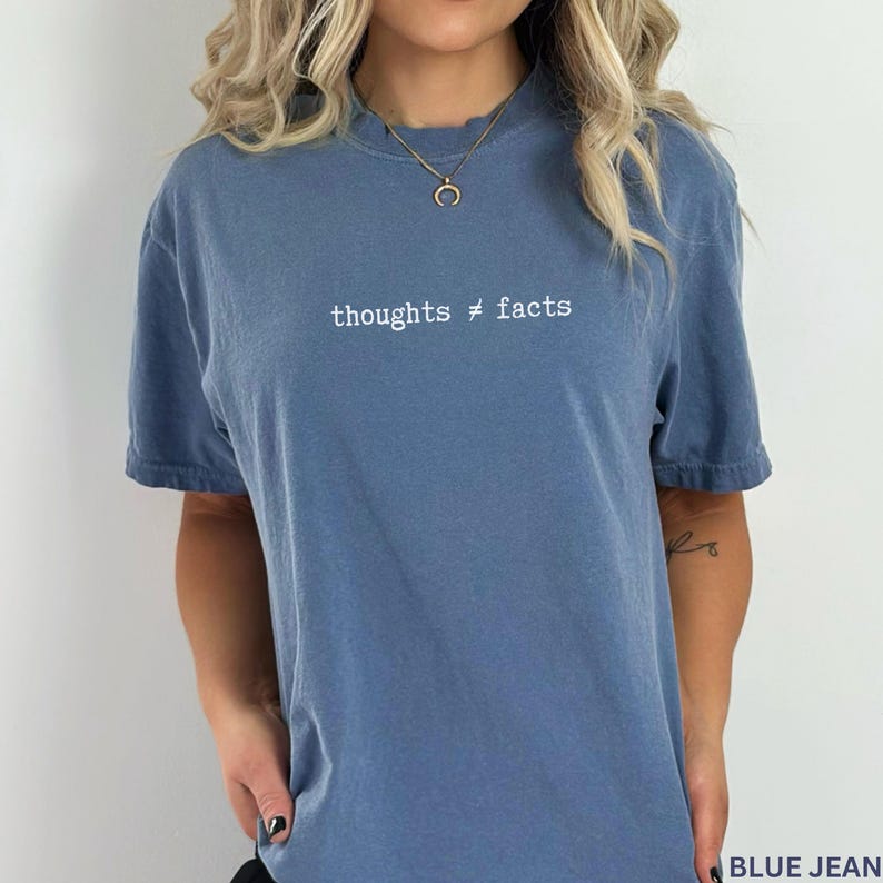 Puede incluir: Camiseta azul con mangas cortas y el texto blanco "thoughts &ne; facts". La camiseta tiene cuello redondo y un aspecto ligeramente descolorido. El color general es un azul apagado.