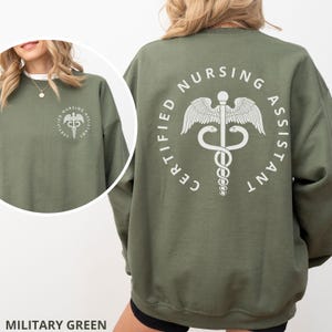 以下が含まれることがあります： 背中に医療シンボルを囲む円の中に「CERTIFIED NURSING ASSISTANT」という文字が書かれた緑色のスウェットシャツです。
