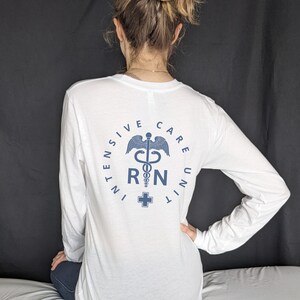 May include: White long-sleeve shirt with a blue graphic of a medical caduceus and the text "INTENSIVE CARE UNIT RN".