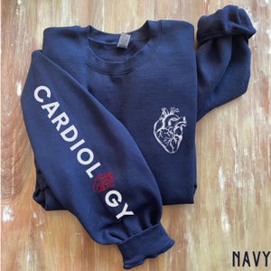 Peut inclure: Sweat-shirt bleu marine avec un graphique de c&oelig;ur anatomique blanc sur le devant et le mot "CARDIOLOGY" en blanc sur la manche gauche.