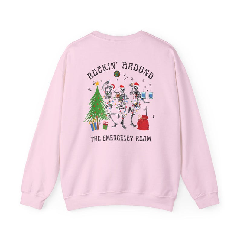 Op de afbeelding: Een lichtroze sweater met ronde hals en een afbeelding op de achterkant van drie skeletten met kerstmutsen die dansen rond een kerstboom met een discobal, cadeautjes en een infuuspaal. De tekst luidt Rockin' Around The Emergency Room.