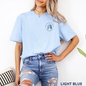 Pode incluir: T-shirt azul claro com gola redonda e mangas curtas. A camisa apresenta um pequeno gr&aacute;fico circular no peito esquerdo com as palavras "Respiratory Therapy" em torno de uma ilustra&ccedil;&atilde;o pulmonar. O texto "LIGHT BLUE" est&aacute; na parte inferior.