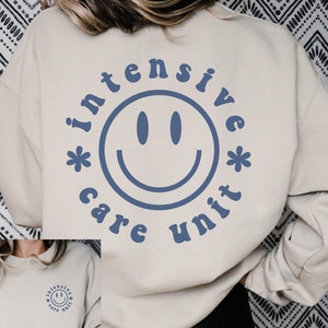 May include: A beige sweatshirt with a blue smiley face graphic and the text "intensive care unit" around the smiley face.