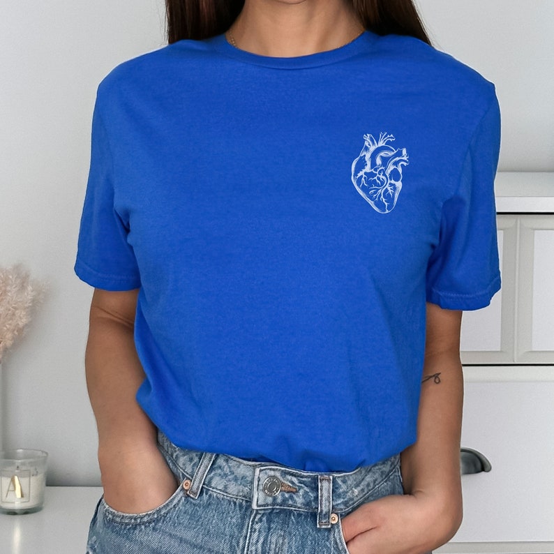 May include: Royal blue t-shirt featuring a white anatomical heart design on the upper left chest. The short-sleeved shirt is made of a soft material and has a classic crew neck.