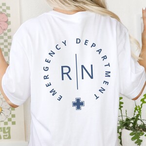 May include: White t-shirt with a navy blue design on the back. The design includes the words "EMERGENCY DEPARTMENT" in a circle around the letters "RN" and a cross symbol. The word "WHITE" is visible at the bottom right.