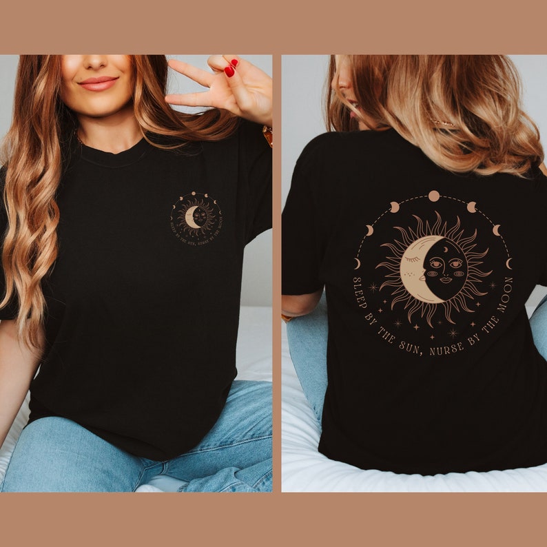 May include: Black t-shirt featuring a celestial design with a sun and moon graphic. The front has a small sun and moon design with the text "Sleep by the sun, nurse by the moon". The back has a larger version of the same design.