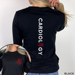 May include: Black long-sleeve shirt featuring the word "CARDIOLOGY" printed vertically in white on the back, with a red anatomical heart graphic below. The shirt also has a small red heart graphic on the front.
