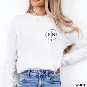 May include: A white long-sleeve shirt featuring a circular navy blue graphic on the left chest. The text inside the circle reads "NEONATAL INTENSIVE CARE UNIT" with "RN" in the center, separated by a vertical line and a small cross symbol below.
