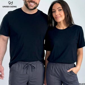 Pode incluir: Duas pessoas vestindo camisetas pretas com gola redonda e cal&ccedil;as cinza com cord&atilde;o. O texto "UNISEX SIZING" est&aacute; acima da imagem. A palavra "BLACK" est&aacute; no canto inferior direito.