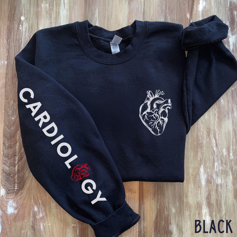 Peut inclure: Sweat-shirt noir avec un graphique de c&oelig;ur anatomique blanc sur le devant et le mot "CARDIOLOGY" imprim&eacute; en blanc sur la manche gauche. La manche pr&eacute;sente &eacute;galement un graphique de c&oelig;ur anatomique rouge.