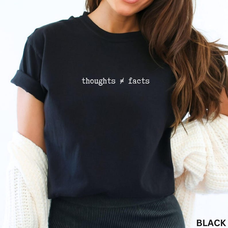 Puede incluir: Camiseta negra con el texto blanco "thoughts &ne; facts". La camiseta de manga corta est&aacute; hecha de un material suave. La camiseta es una prenda informal.