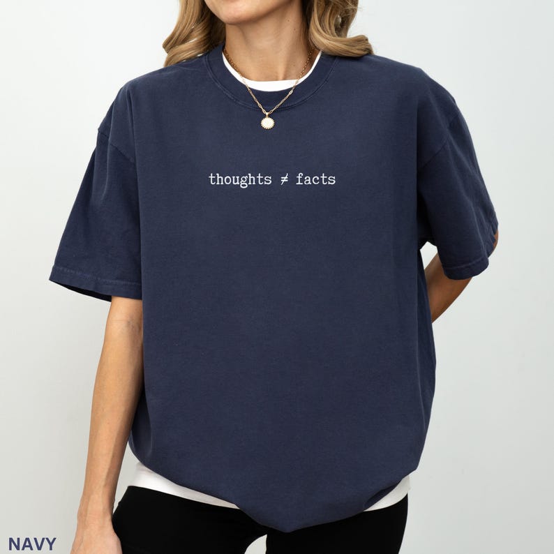 Puede incluir: Camiseta azul marino de manga corta con el texto blanco "thoughts &ne; facts". La camiseta tiene un corte holgado y cuello redondo. La persona lleva un collar dorado.