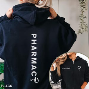 May include: Black hoodie with the word "PHARMACY" printed vertically in white on the back. The hoodie also features a pharmacy symbol at the bottom of the word. A smaller image shows a black zip-up hoodie with the name "Elizabeth CPhT" and a pharmacy symbol.