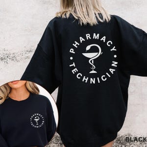 May include: Black sweatshirt with white text and a pharmacy symbol. The words "PHARMACY TECHNICIAN" are in a circular design on the back. A smaller version of the design is on the front of the sweatshirt. The sweatshirt is a crew neck style.